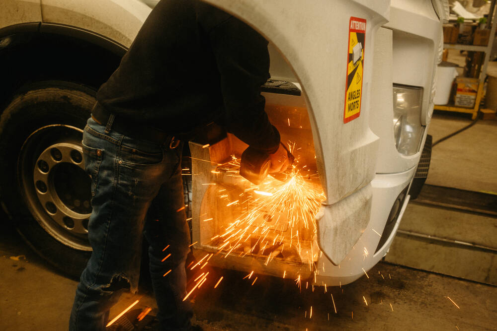 Ein Werkstattmitarbeiter trennt mit einer Flex ein Stück der LKW-Treppe ab; dabei fliegen Funken.
